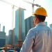 New York Construction Manager supervising an active construction site in Manhattan with cranes and blueprints.